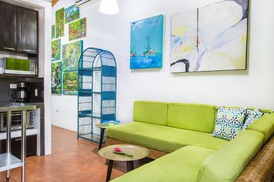 Bright living room with lime-green sectional, wall art, blue shelf, and small round coffee table