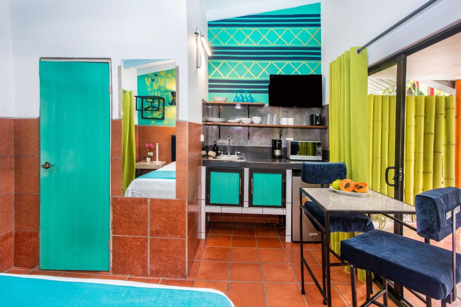Modern kitchen and dining nook with turquoise accents, terracotta floor, and small table by a curtained window