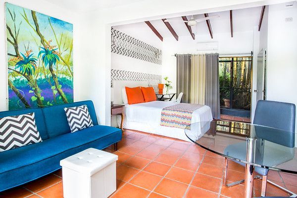Bright studio room with blue sofa, bed, glass table, and orange tile floor