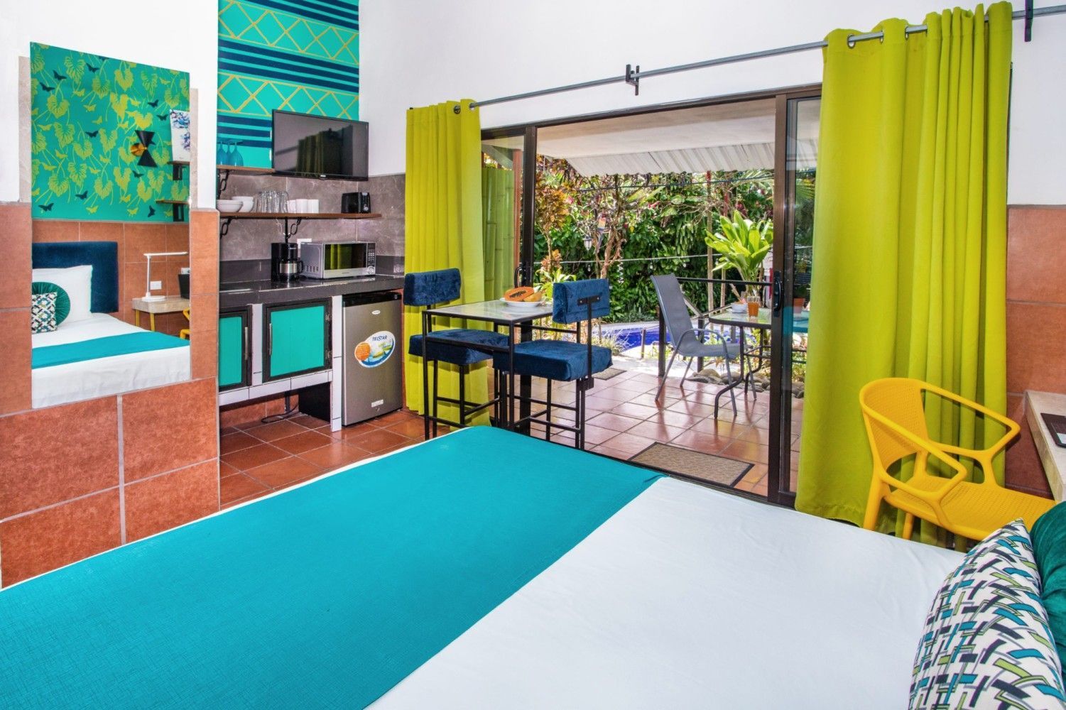 Colorful bedroom with turquoise bedspread, lime curtains, desk, and a sliding glass door to a balcony