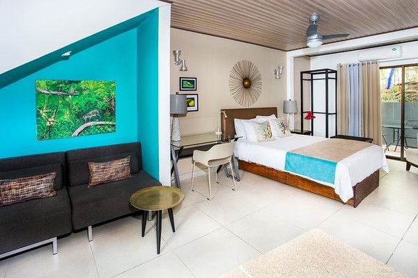 Modern hotel room with a bed, sofa, desk, and tropical decor