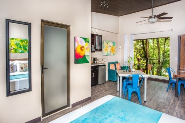 Bright living room with blue chairs, colorful art, and large sliding glass doors to greenery