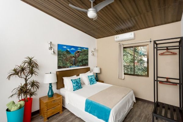 Cozy bedroom with white bed, teal accents, wood ceiling, window, lamp, and open clothes rack