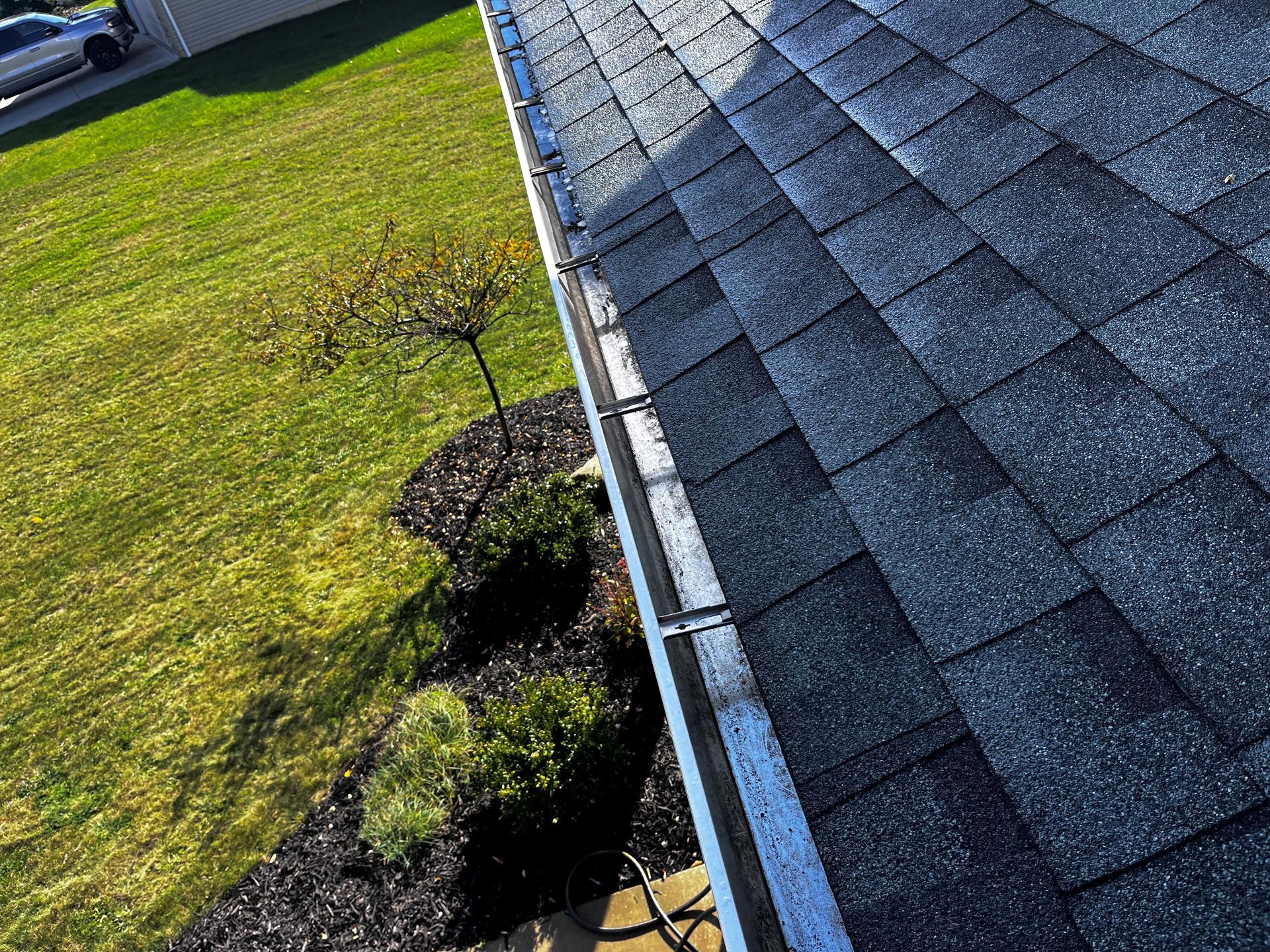 A person wearing blue gloves is cleaning a gutter on a roof.