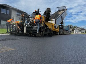 Des ouvriers pavant une rue résidentielle à l'aide d'une machine à paver et d'un rouleau compresseur d'asphalte.