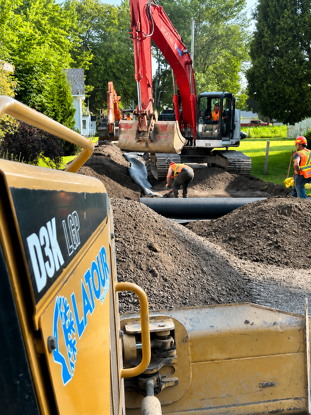Chantier de construction avec une excavatrice en train de creuser à côté d'un grand tas de terre et des ouvriers en équipement de sécurité.