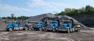 Quatre camions-bennes bleus étaient stationnés dans une gravière, avec un gros tas de pierres concassées derrière eux.