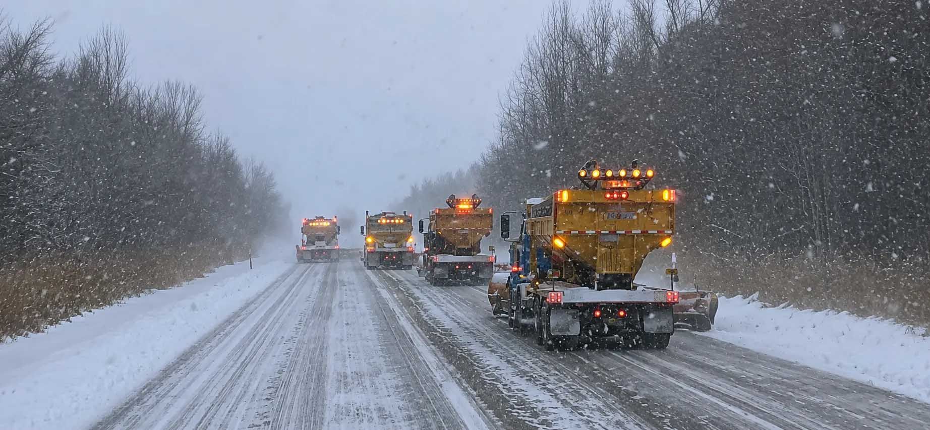 Des chasse-neige dégagent une autoroute enneigée lors d'une forte tempête de neige, les véhicules roulant prudemment.
