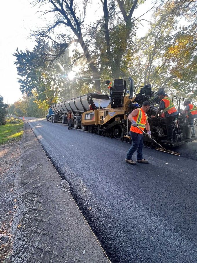 Une équipe de travailleurs routiers travaille à côté d'un camion-citerne en train de paver une route rurale au lever du soleil.