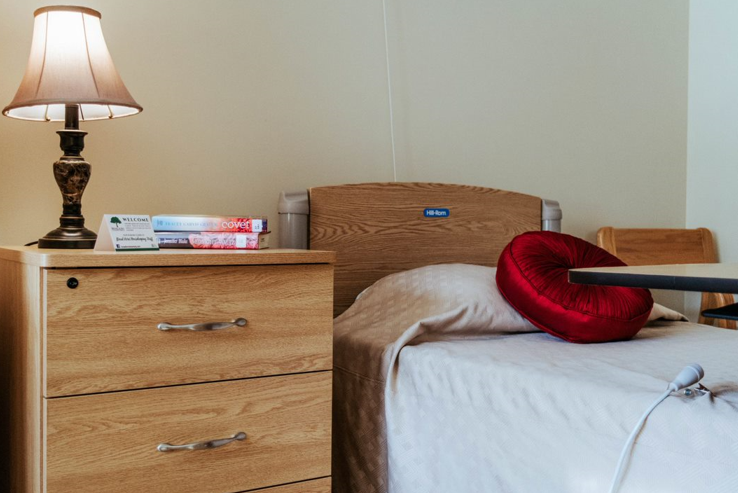 Bedroom with wooden nightstand, bed, lamp, and red heart-shaped pillow.
