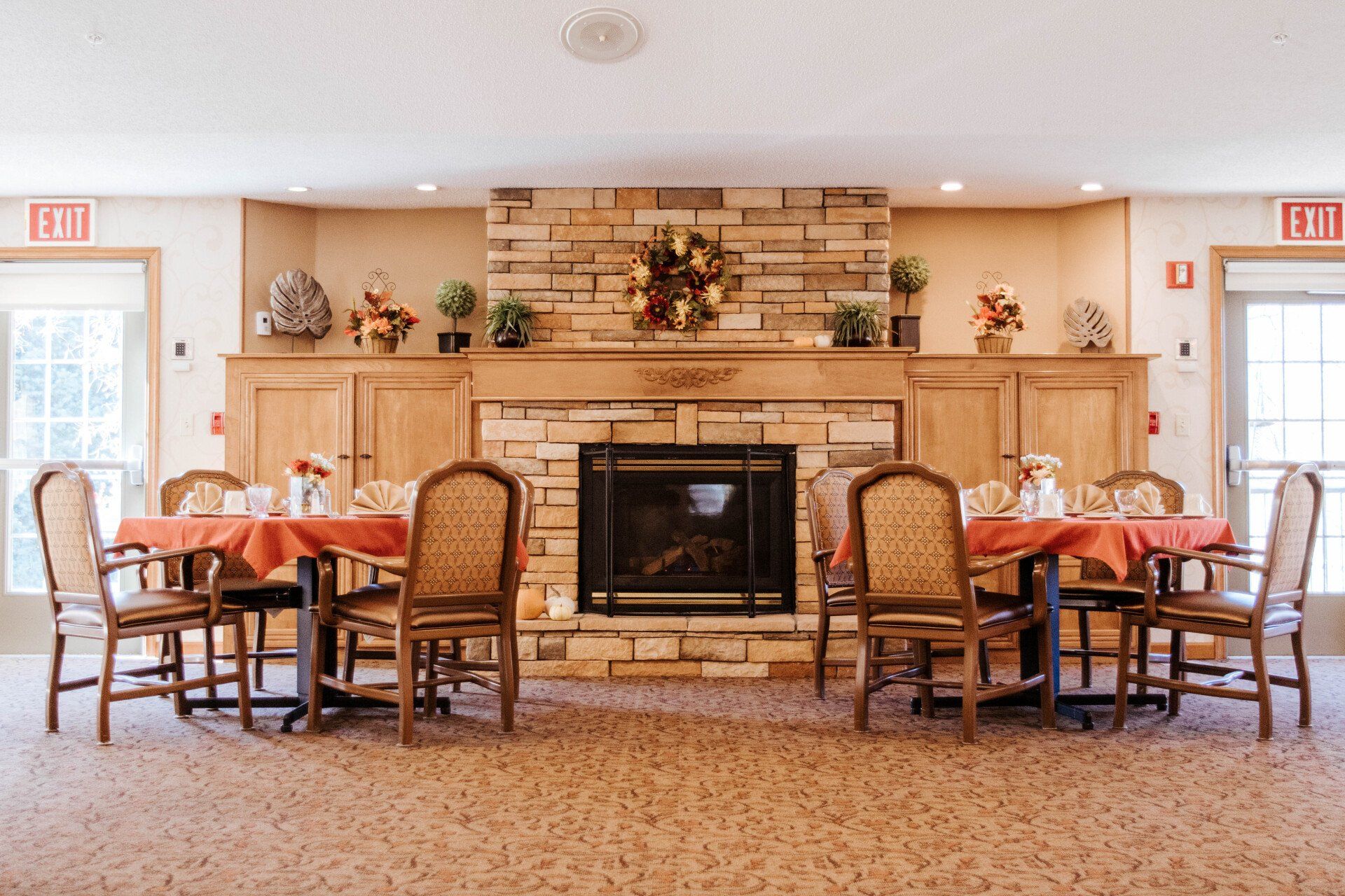 Dining room with fireplace, tables with red tablecloths, wood chairs, beige carpet, and neutral walls.