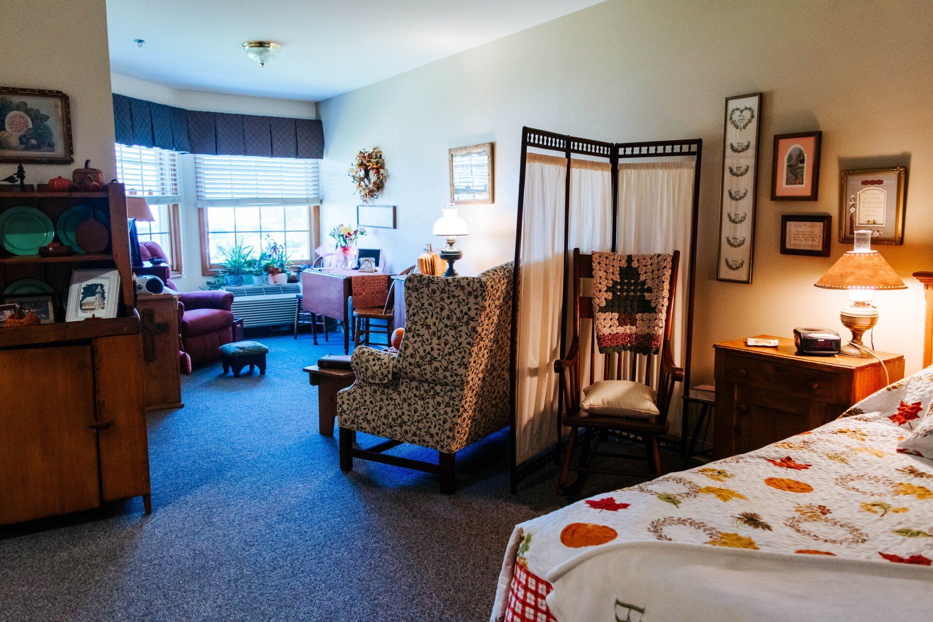 Cozy senior living apartment: living area with armchair, screen divider, bed, and decorative items.