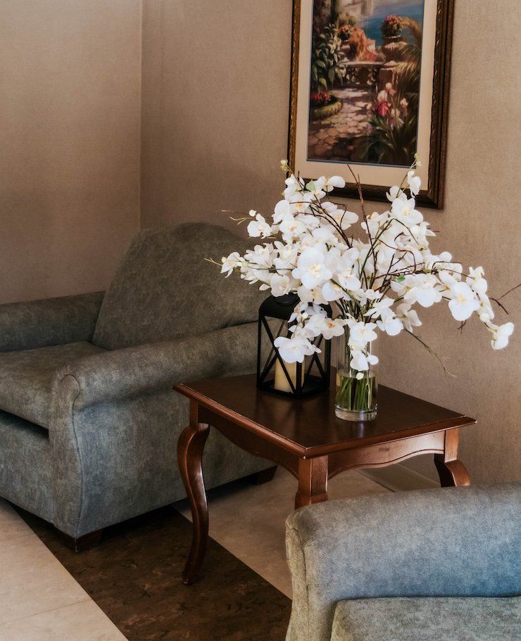 Two gray armchairs with a small table holding white flowers and a framed painting.