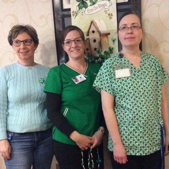 Three people wearing green near a decorative sign, celebrating St. Patrick's Day.