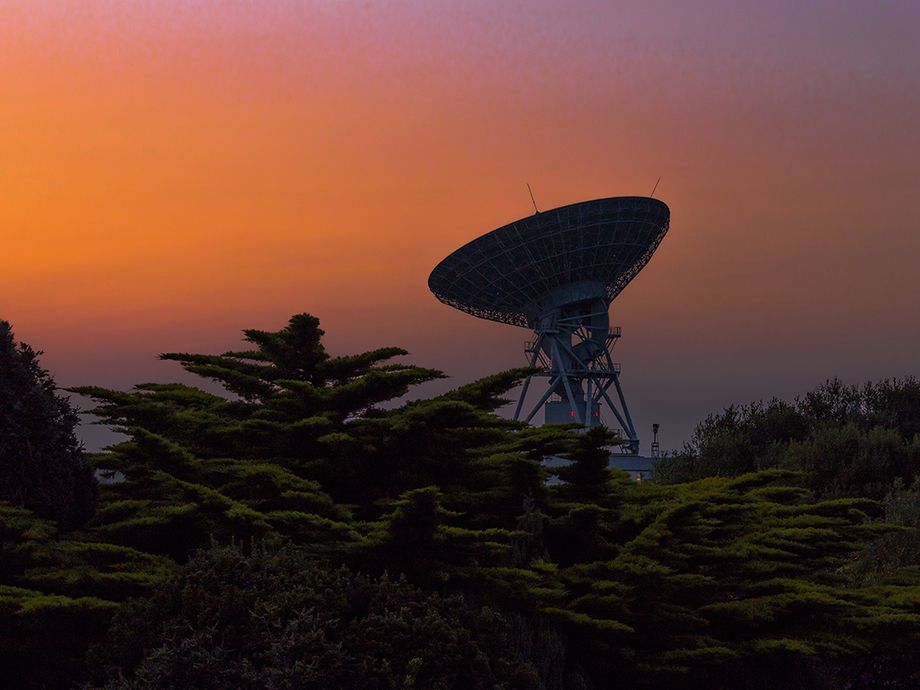 Photo showing Goonhilly's Deep Space antenna GHY6 silhouetted against the deep reddish orange colours of late evening sunset