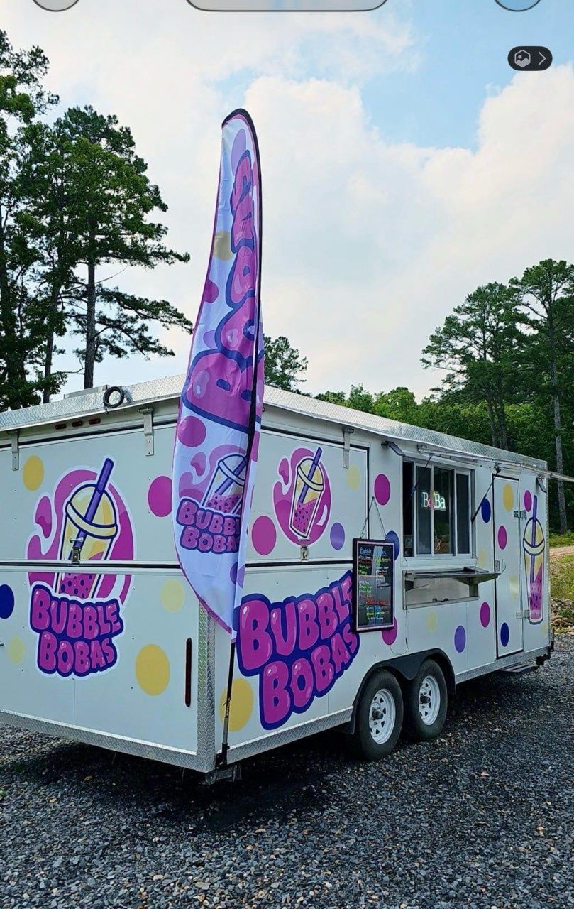 Bubble tea-themed food trailer with pink and purple graphics parked on gravel outdoors
