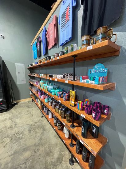 Retail display shelves with colorful bottles and cans on a gray wall in a store.