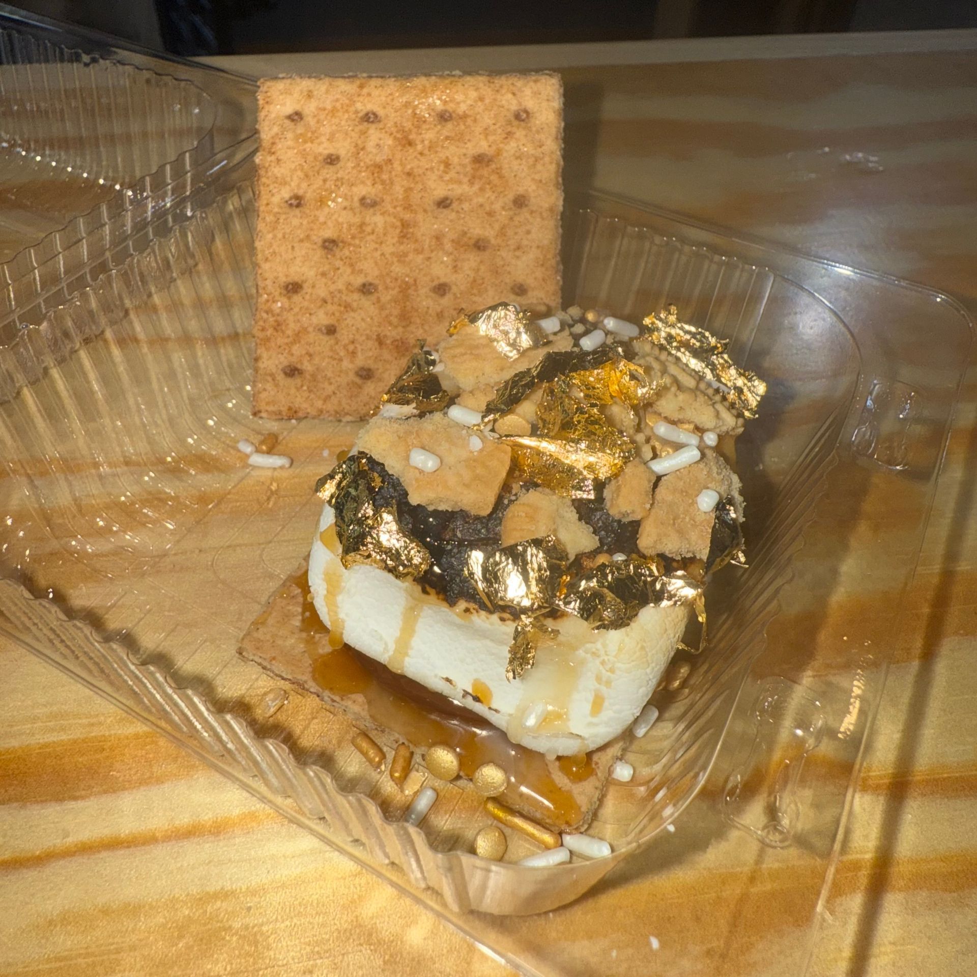 Marshmallow dessert topped with crushed graham crackers and chocolate on a plastic tray with a cracker behind it