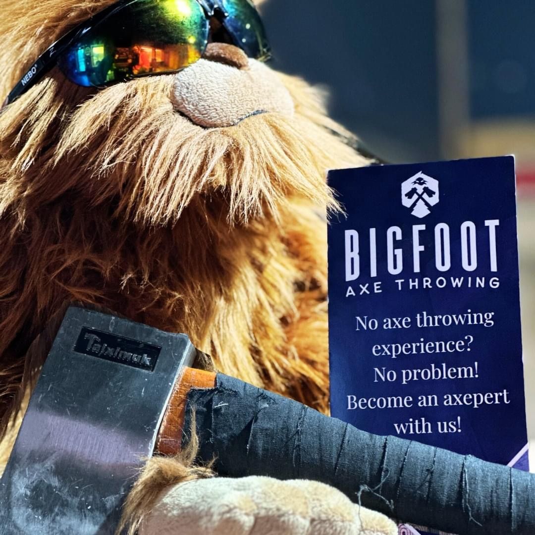 Stuffed lion wearing sunglasses holds a Bigfoot axe throwing promo card and a sign.