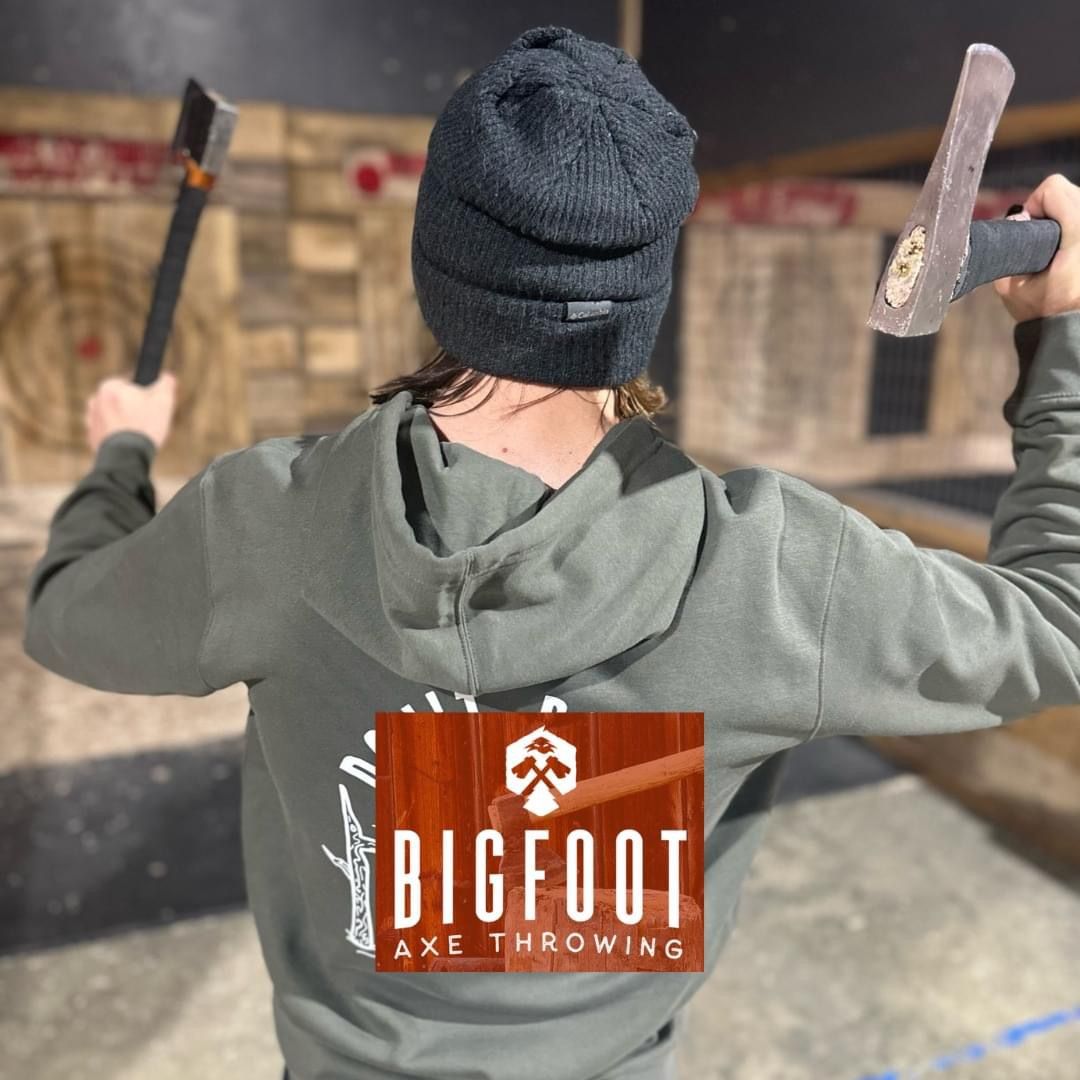 Person in a black beanie throws axes at a target in an indoor Bigfoot Axe Throwing venue.