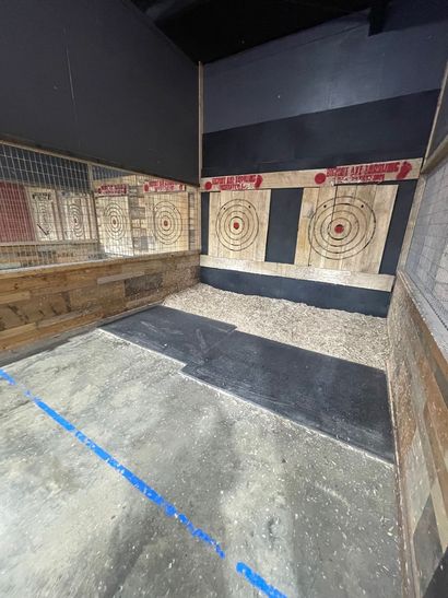 Indoor axe-throwing lane with wooden target boards, gravel floor, and blue tape line