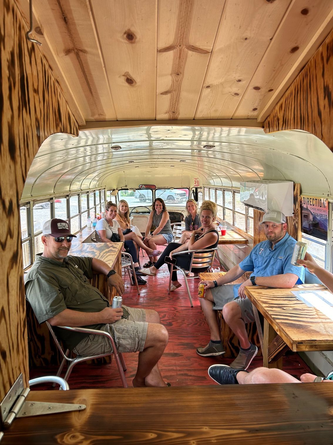 People seated inside a vintage bus-like vehicle, smiling and chatting on a sunny ride.