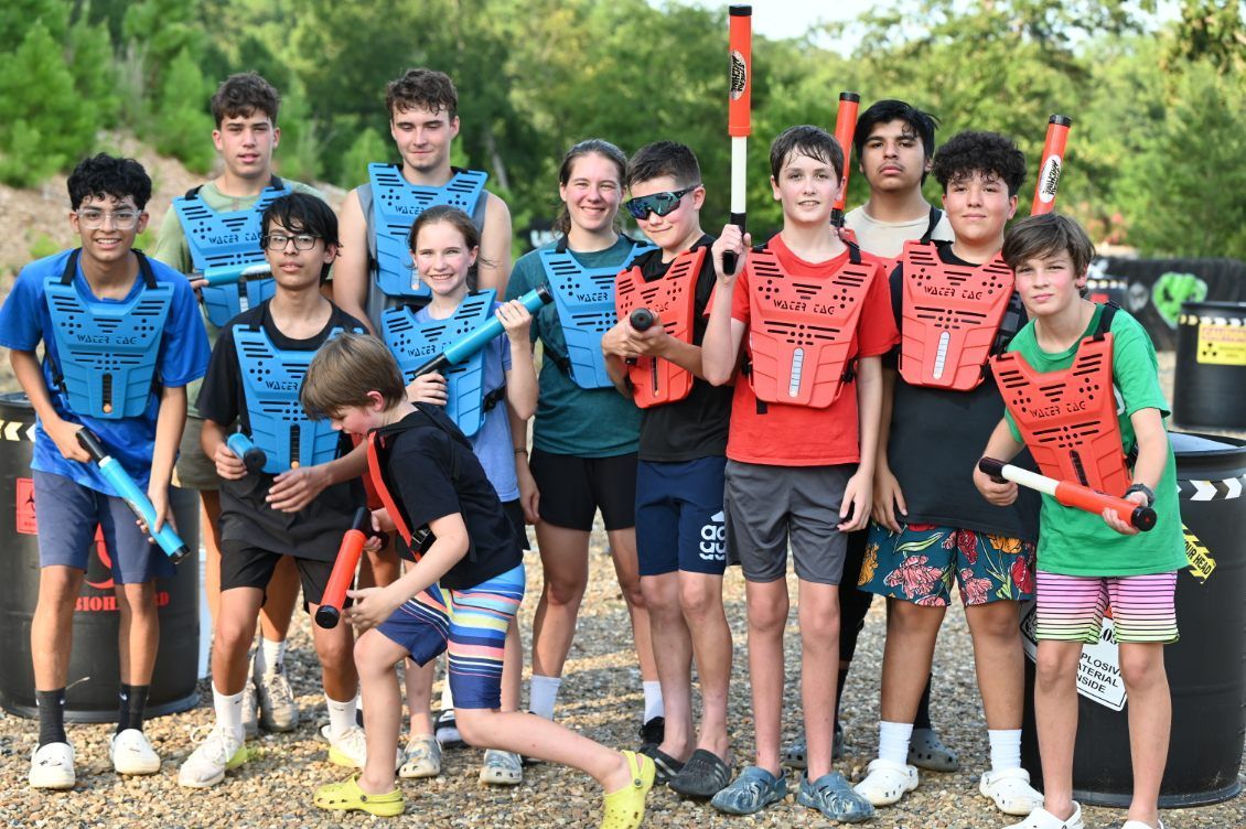 Group of kids and teens posing outdoors with colorful paintball markers and gear