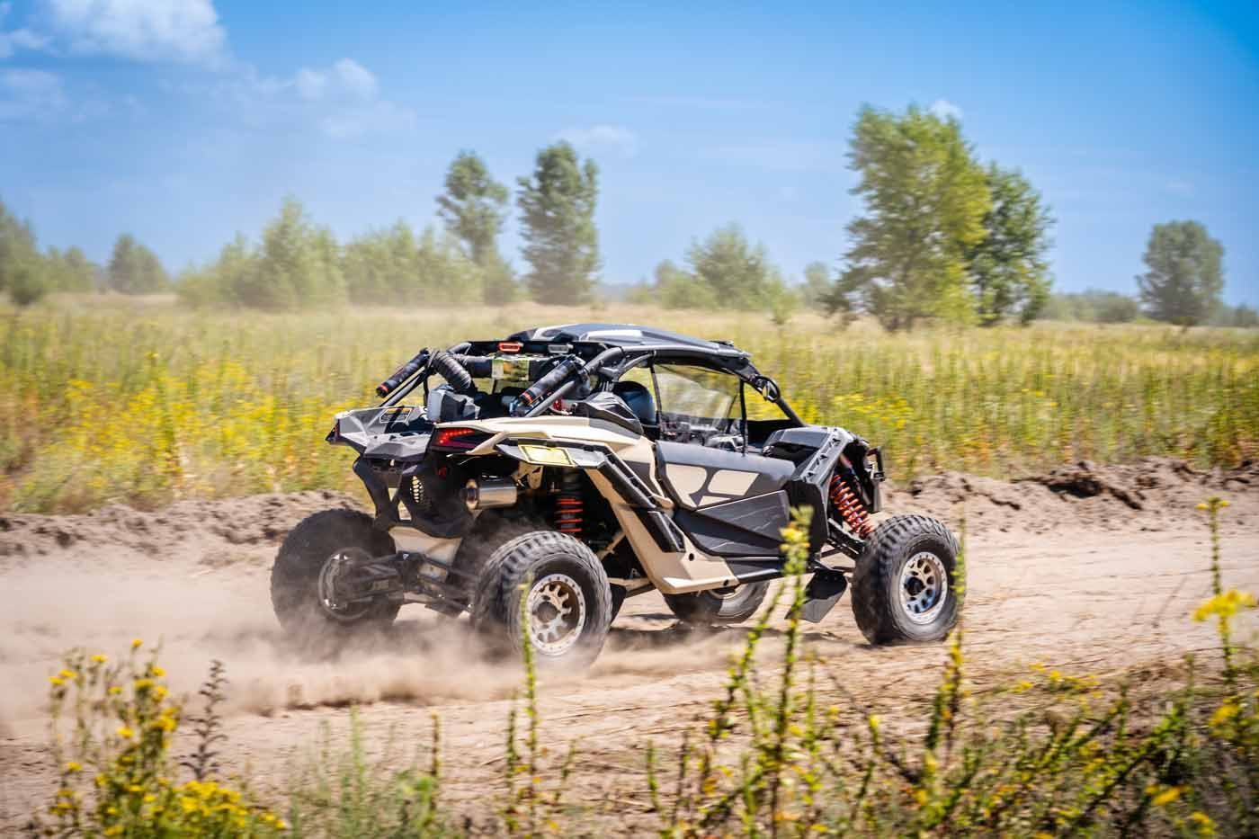 Off-road dune buggy kicking up dust on a sandy trail beside yellow wildflowers under a blue sky