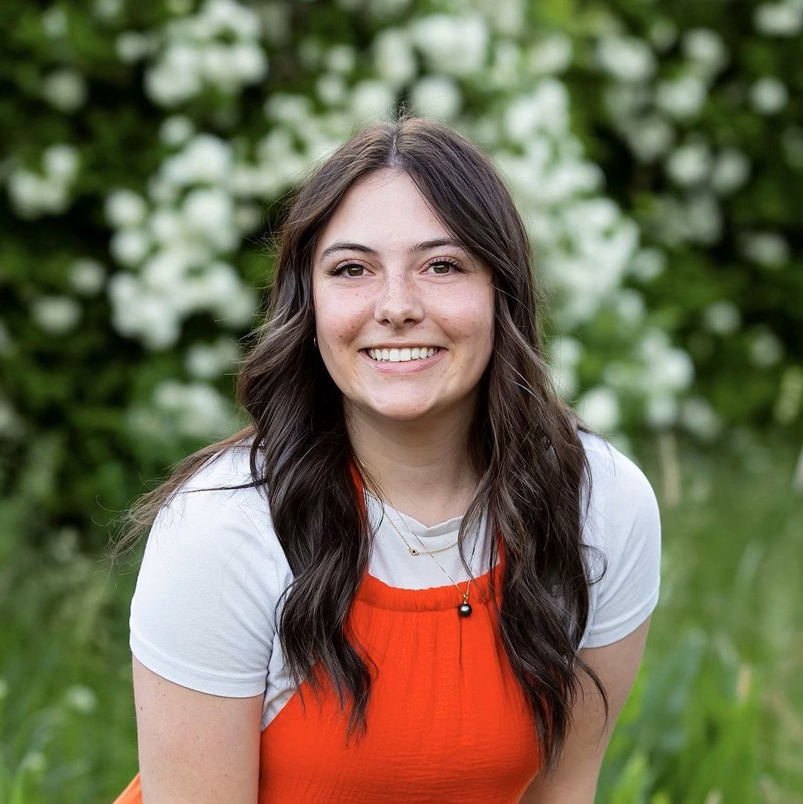 A woman in an orange dress and white shirt is smiling for the camera.