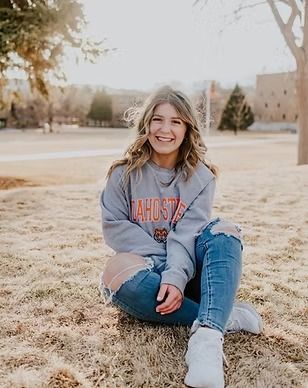 A woman is sitting on the grass wearing a sweatshirt and ripped jeans.