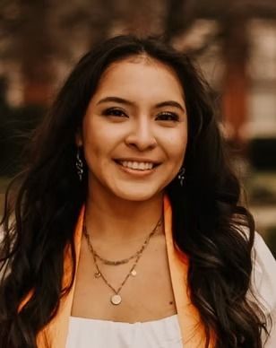 A close up of a woman wearing a graduation cap and gown and smiling.