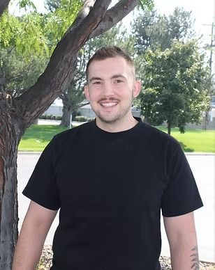 A man in a black shirt is standing in front of a tree.
