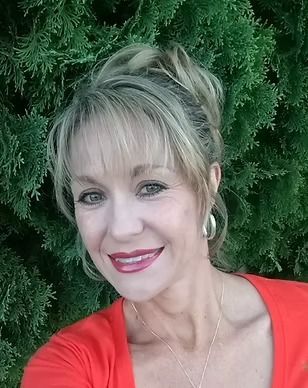 A woman in a red shirt is smiling in front of a tree.