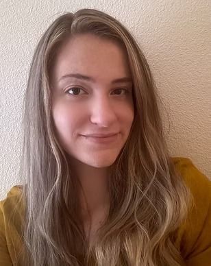 A woman with long blonde hair is smiling and wearing a yellow sweater.