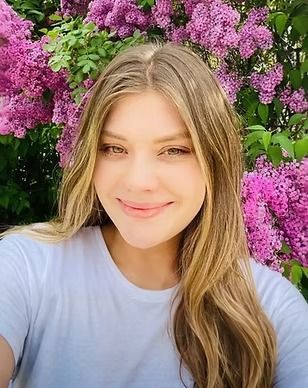 A woman is taking a selfie in front of a bush of purple flowers.