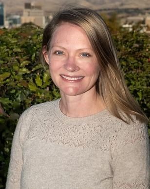 A woman in a white sweater is smiling in front of a bush.