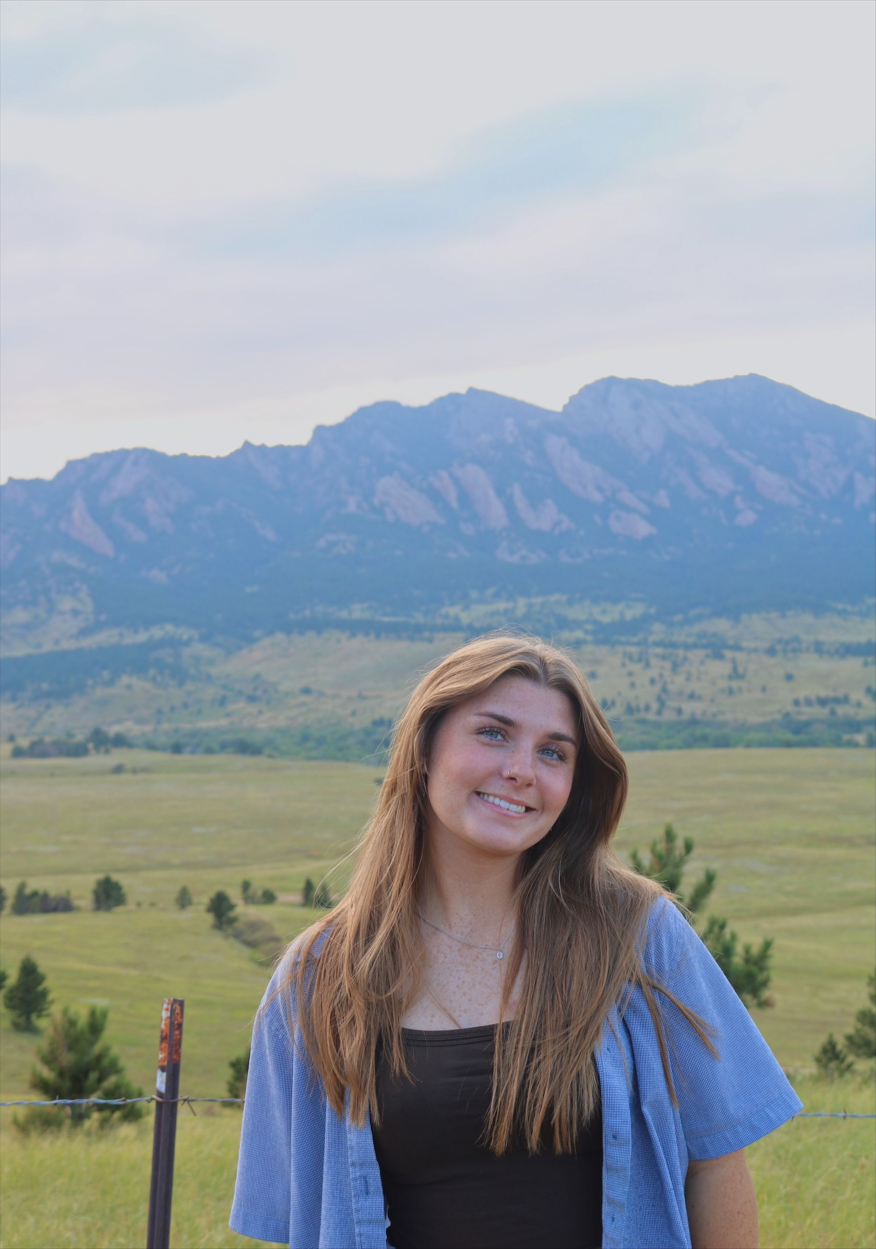 A young woman in a blue dress is smiling in a field of flowers.