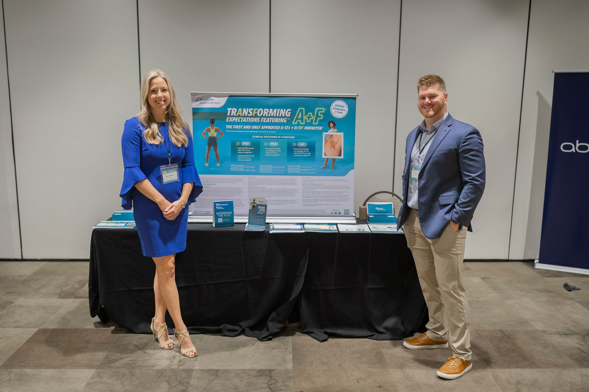 Two people stand beside a conference booth with a blue product display and table