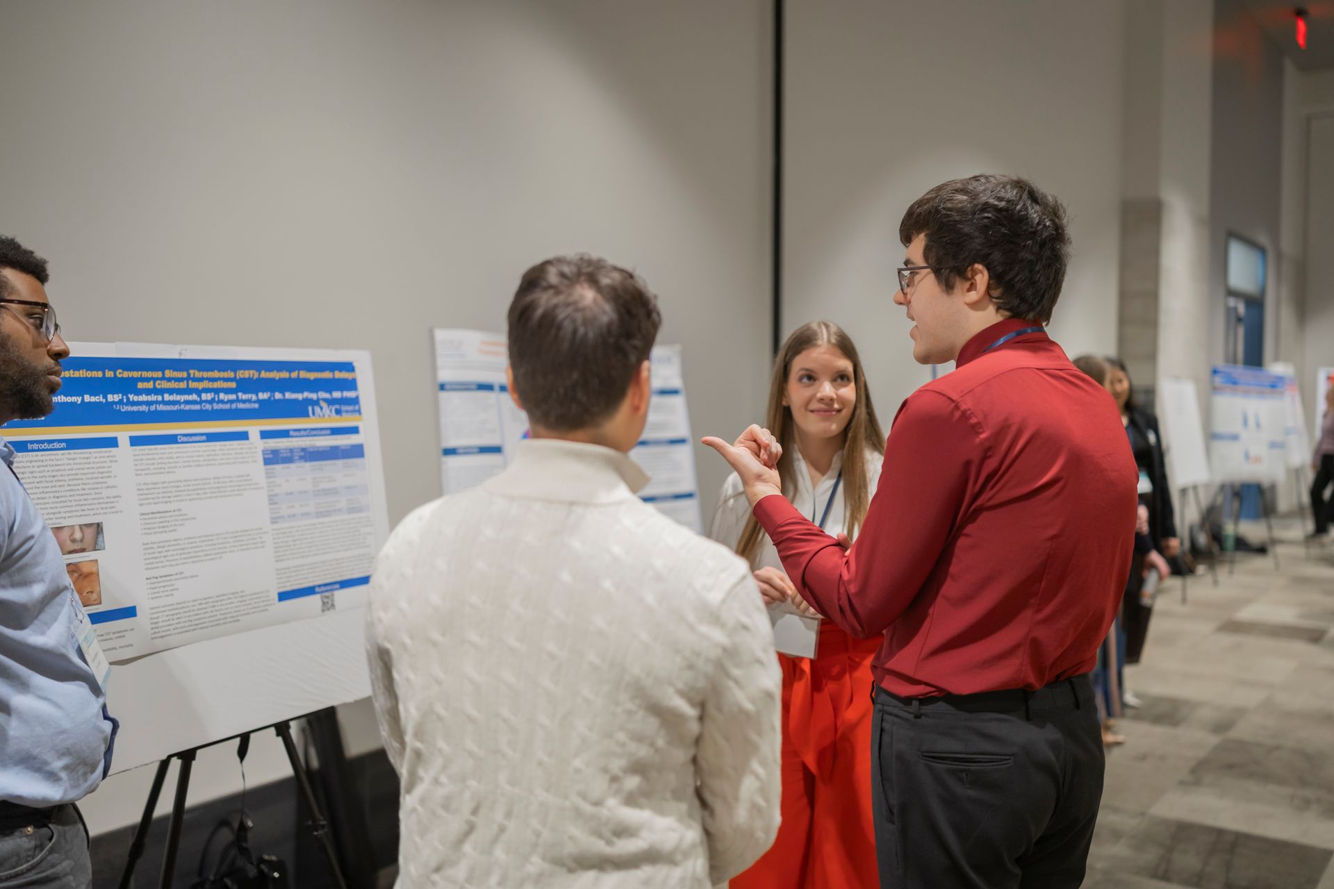 People discussing a poster presentation at a conference, with a woman in red speaking to attendees.