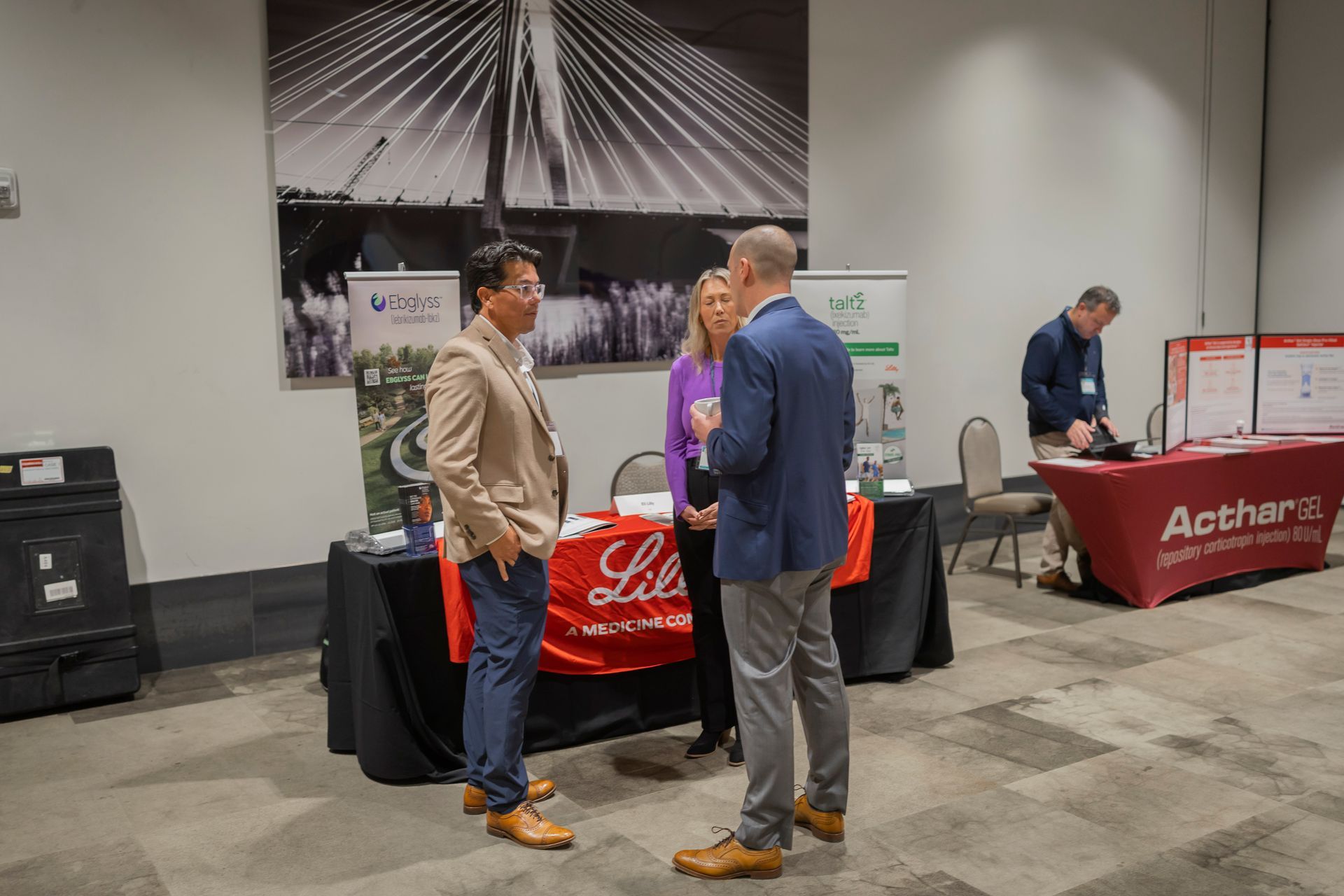Trade show booth with two men talking beside red-and-black display tables in a convention hall