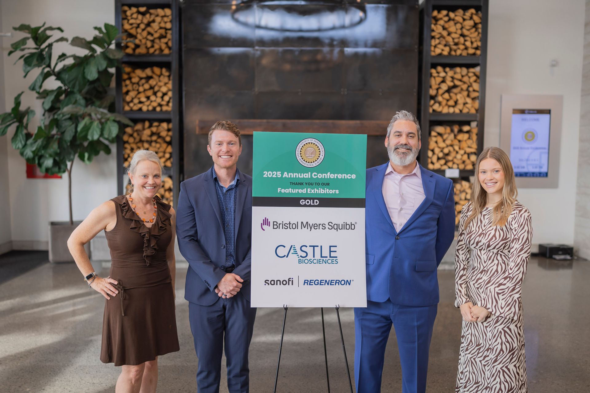 Four people stand in a lobby holding a CASTLE sign and smiling in front of a green event banner.
