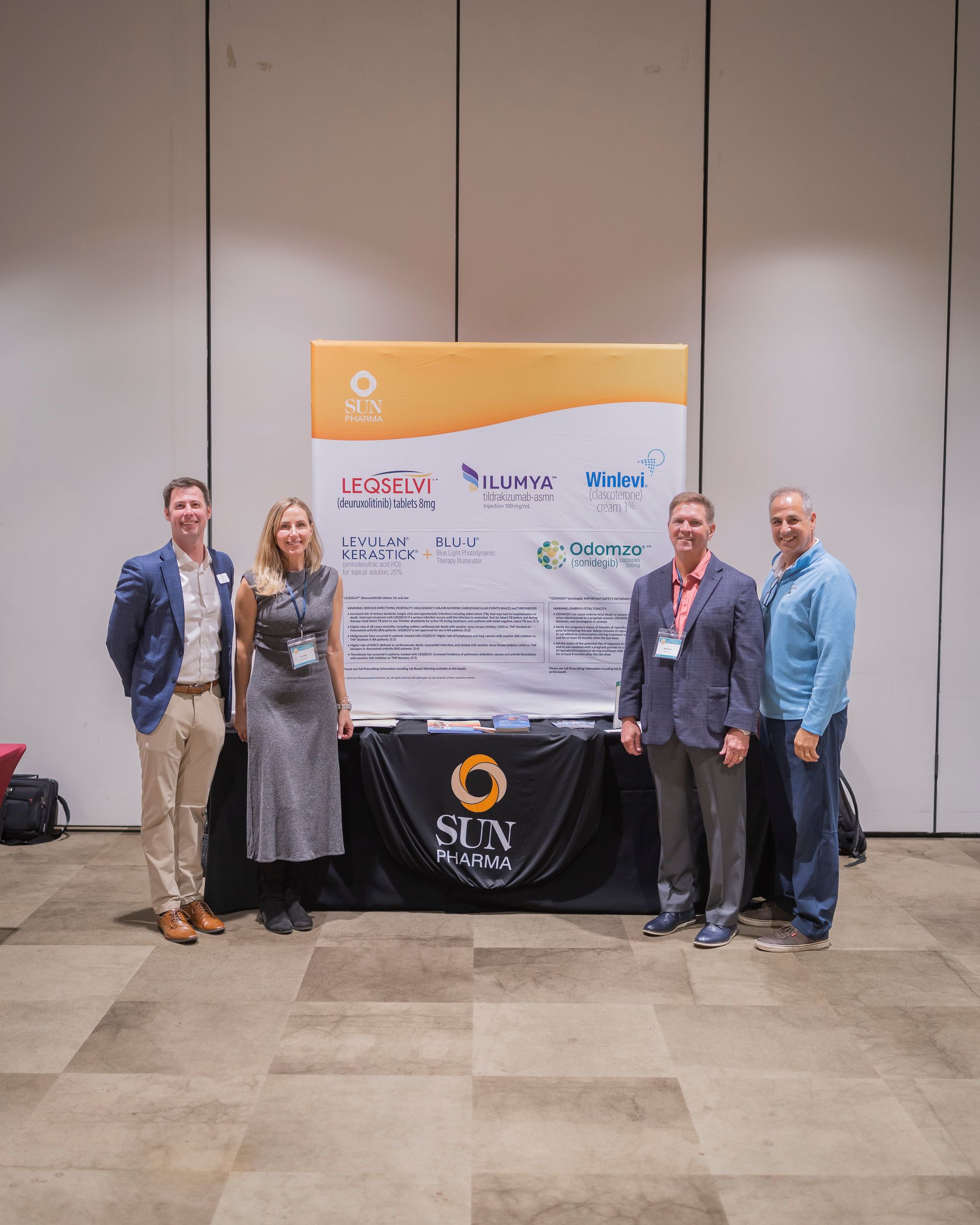 Five people pose beside a branded event banner and table in a conference hall.