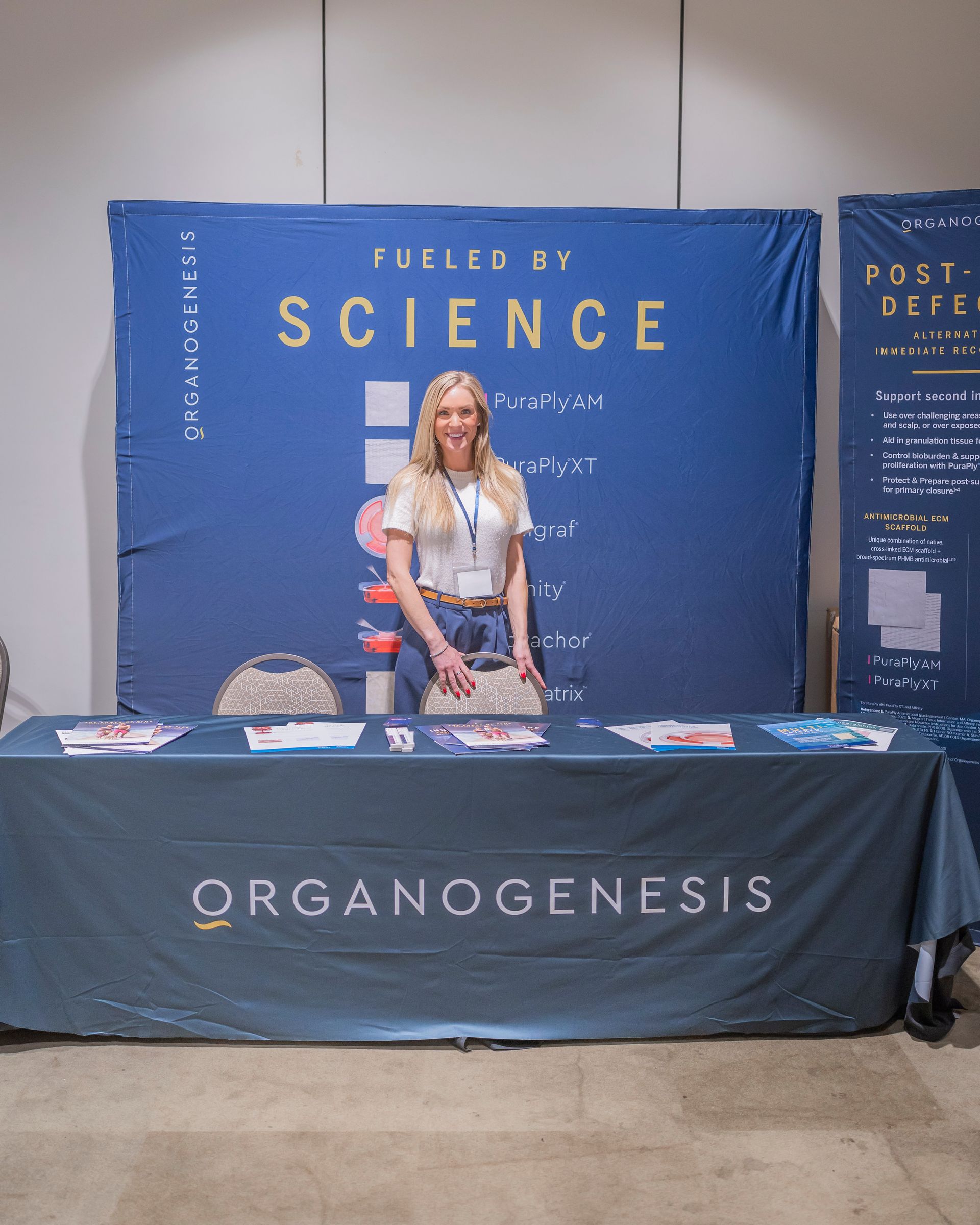Woman at an Organogenesis booth with a blue “Fueled by Science” backdrop and table banner.