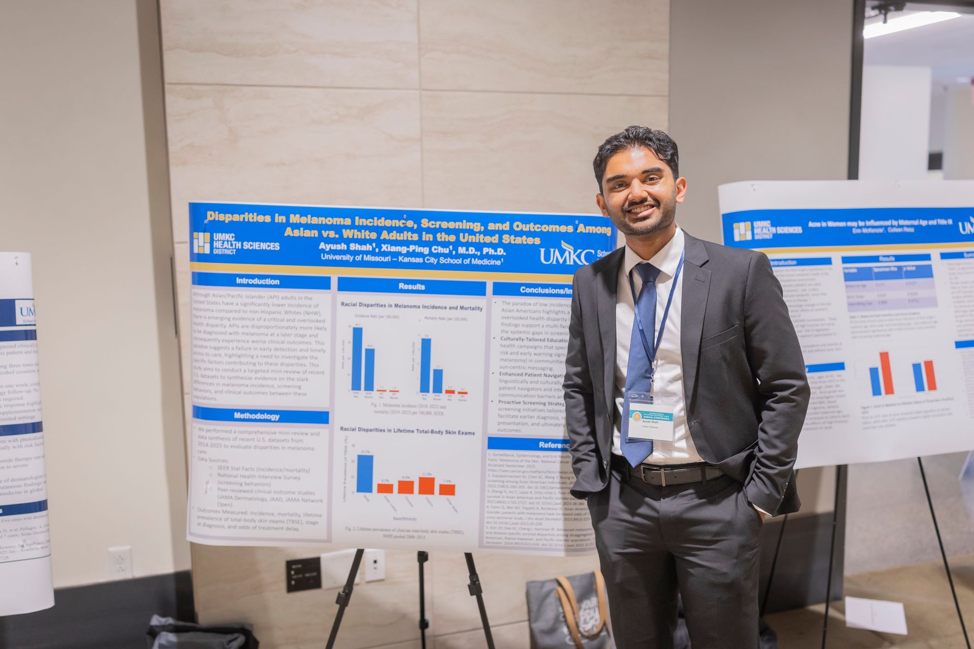 Man in a suit standing beside scientific poster boards with charts at a conference booth