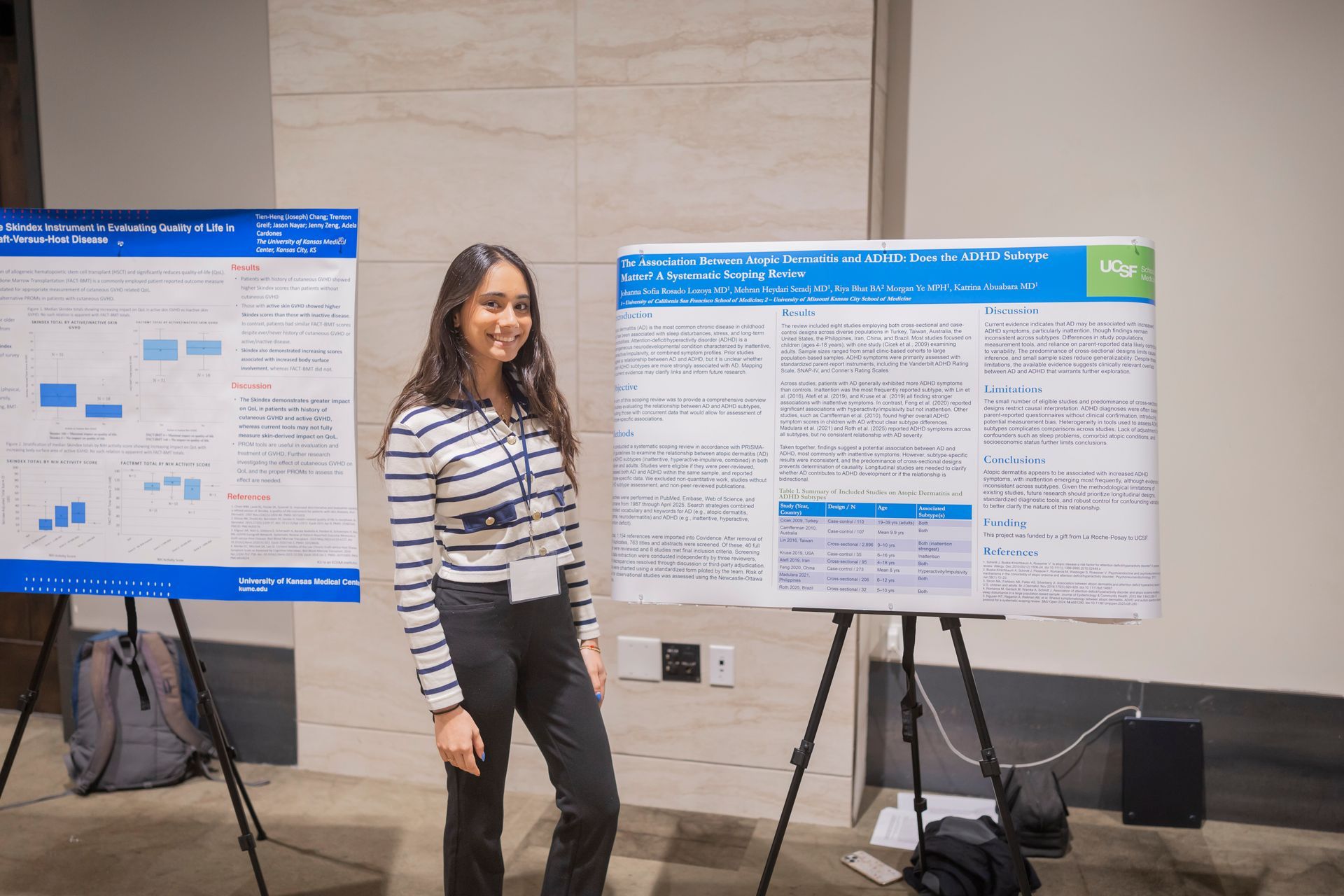 Woman standing beside two poster presentations on easels in a conference hall.