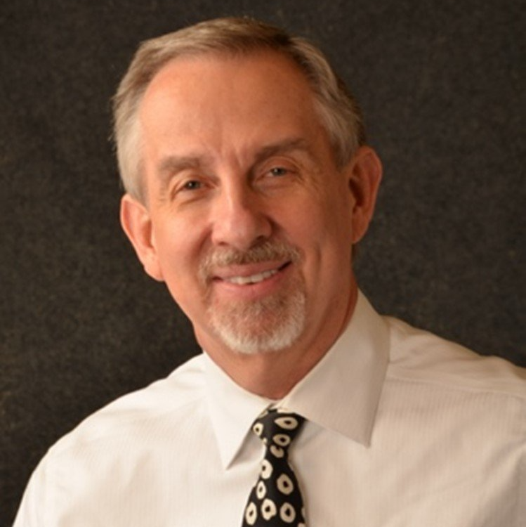 A man in a white shirt and black tie smiles for the camera