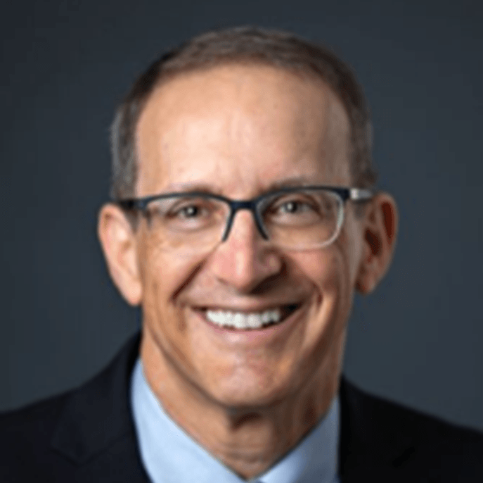 A man wearing glasses and a suit smiles for the camera