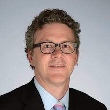 A man wearing glasses and a suit and tie is smiling for the camera.