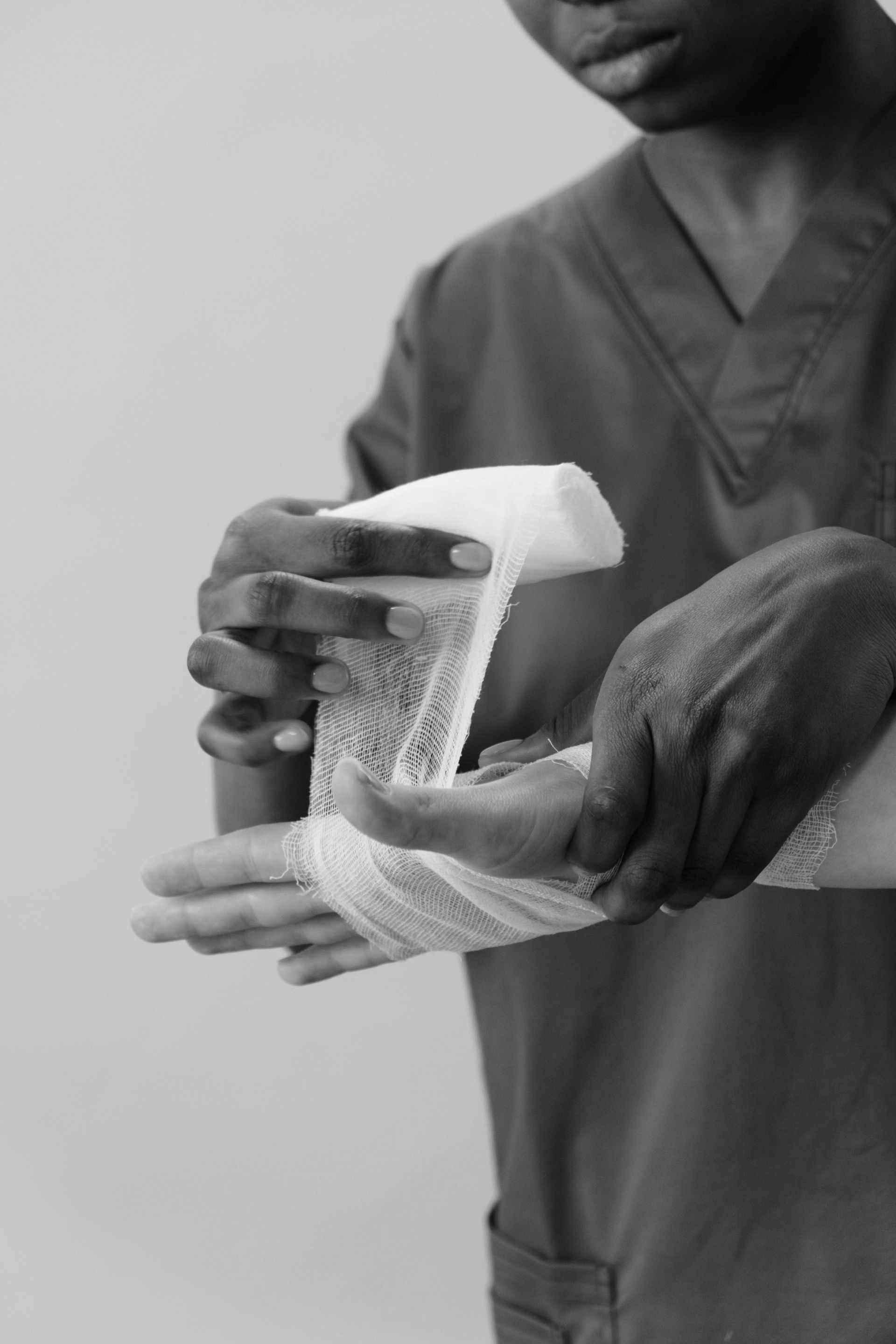 Person wrapping a white bandage around a hand, likely in a medical setting.