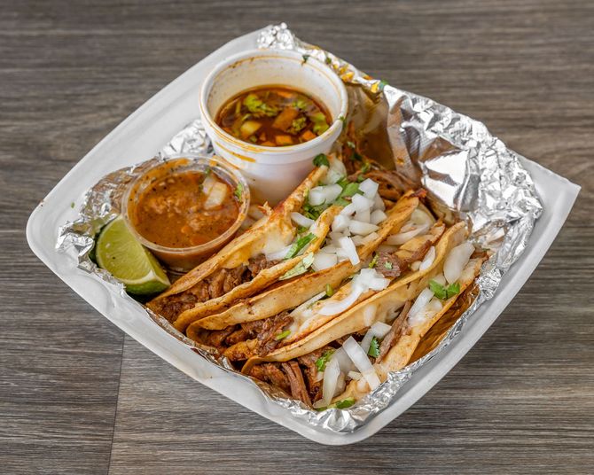 Grilled chicken wrap with sauces, lemon wedge, and vegetables served in a foil tray